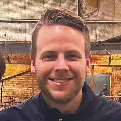 Alex Johnson, a White man with a stubble beard and parted sandy-brown hair, smiling, wearing a black jacket