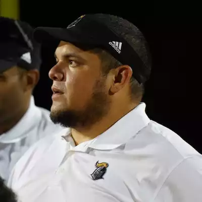Gio De La Peña, a man with a Lincoln beard, wearing a black Adidas visor, and a white polo shirt, looking to the left.