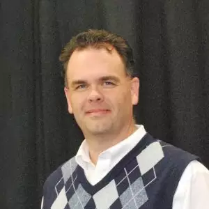 Jay Stancil, a White man with dark combed-back hair, weaaring a sweater vest over a white dress shirt.